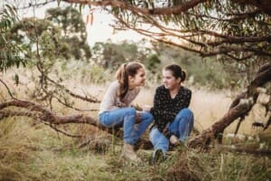Sisters sit on a low tree branch at sunset