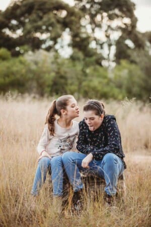 A girl tries to kiss her sister on the cheek, her sister pulls a face