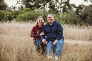 Parents sit on a log and laugh at sunset