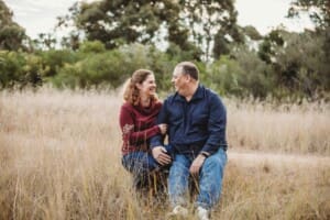 A couple sit on a log in a grassy field and hug