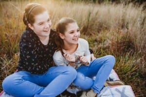 Sisters sit in long grass and cuddle at sunset