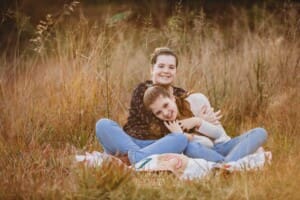 Sisters sit on a rug in long grass and hug