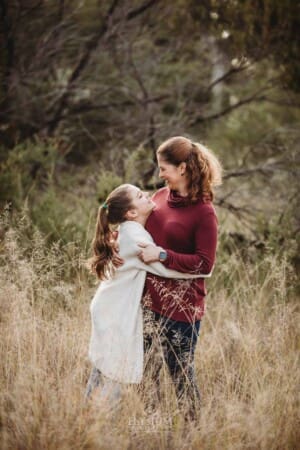 A mother and daughter stand cuddling in long grass