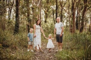 A family stand on a bush path holding hands