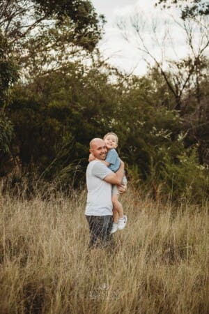 A father hugs his son as they stand in long grass