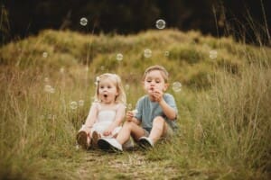 A little girl gasps as her brother blows bubbles next to her