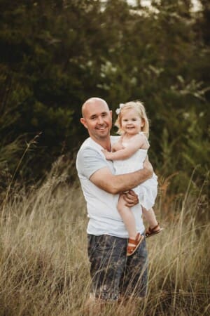 A father hugs his little girl as they stand in long grass