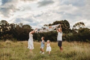 Parents lift a colourful rug above their kids as they play in a grass field