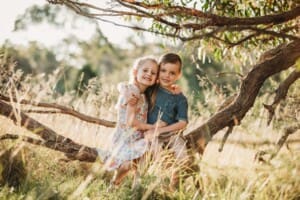 Children sit on a low tree branch at sunset