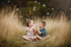 2 children sit in long grass and blow bubbles