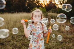 A little girl blows bubbles at sunset in a field