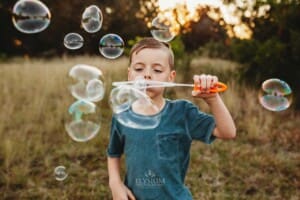 A little boy blows bubbles at sunset in a field