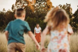 A mother stands in long grass as her children race toward her