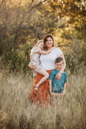 A mother hugs her children standing in long grass