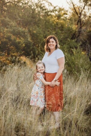 A little girl standing in long grass hugs her mother