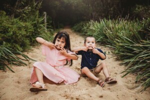 Children sit on a sandy beach path and pull funny faces