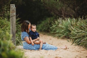 A mother sits cuddling her son on a sandy beach path