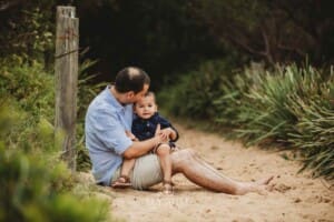 A father sits cuddling his son on a sandy beach path