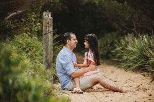 A father sits cuddling his daughter on a sandy beach path