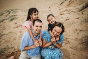 Children cuddle their parents as they sit in the sand at a beach