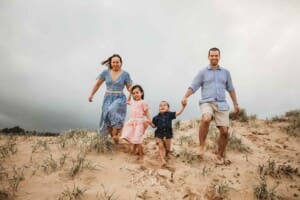 Parents hold hands with their children as they all run down a sand dune