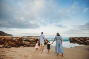 Parents hold hands with their children as they stand on the beach