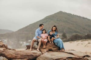 A family sit on rocks at the beach with hills behind them