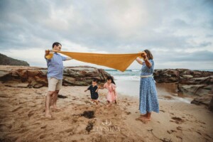 Parents hold a yellow blanket between them as their kids run under it