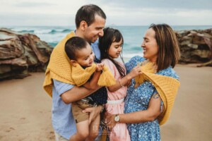 Parents cuddle their children between them wrapped in a yellow blanket