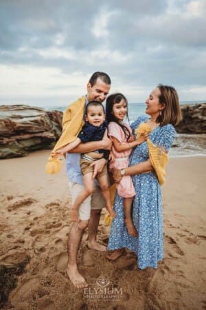 Parents cuddle their children between them wrapped in a yellow blanket