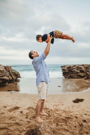 A dad lifts his son above him on the beach