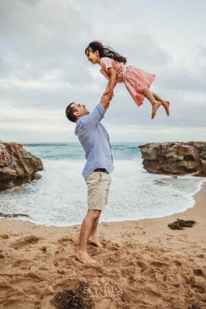 A dad lifts his daughter above him on the beach