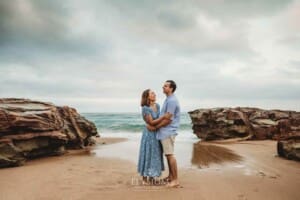 Parents cuddle each other while standing on a beach