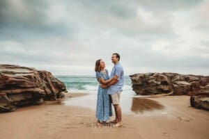 Parents cuddle each other while standing on a beach