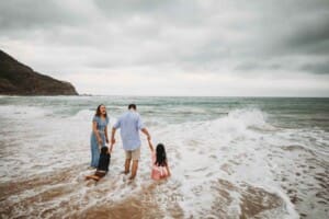 Parents hold hands with their kids as they play in the water at the beach