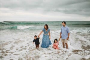 Parents hold hands with their kids as they play in the water at the beach