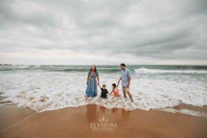 Parents hold hands with their kids as they play in the water at the beach