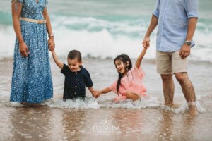 Parents hold hands with their kids as they play in the water at the beach