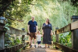 Parents hold their son's hands as he stands between them