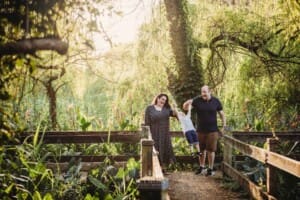 Parents stand on a boardwalk and swing their son between them