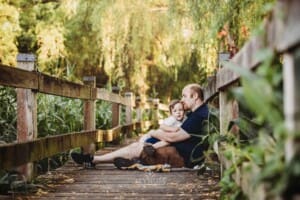 A little boy cuddles his dad as they sit on a boardwalk