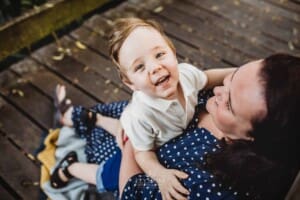 A little boy cuddles his mum as they sit on a boardwalk