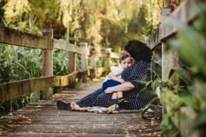 A little boy cuddles his mum as they sit on a boardwalk