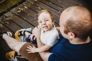 A little boy sits with his dad on a boardwalk