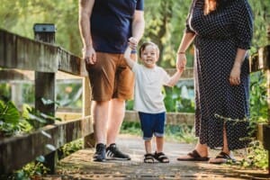 Parents hold their son's hands as he stands between them
