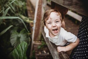 A little boy leans through a boardwalk railing and smiles