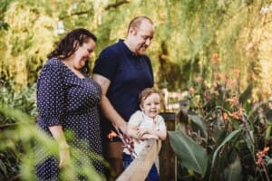 A little boy stands on a boardwalk with his parents