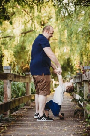 A dad standing on a boardwalk plays with his son
