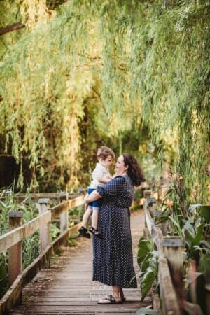 A little boy cuddles his mum as they stand on a boardwalk