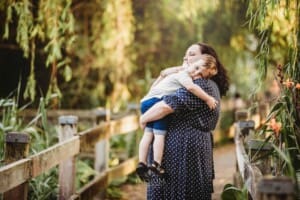 A little boy cuddles his mum as they stand on a boardwalk
